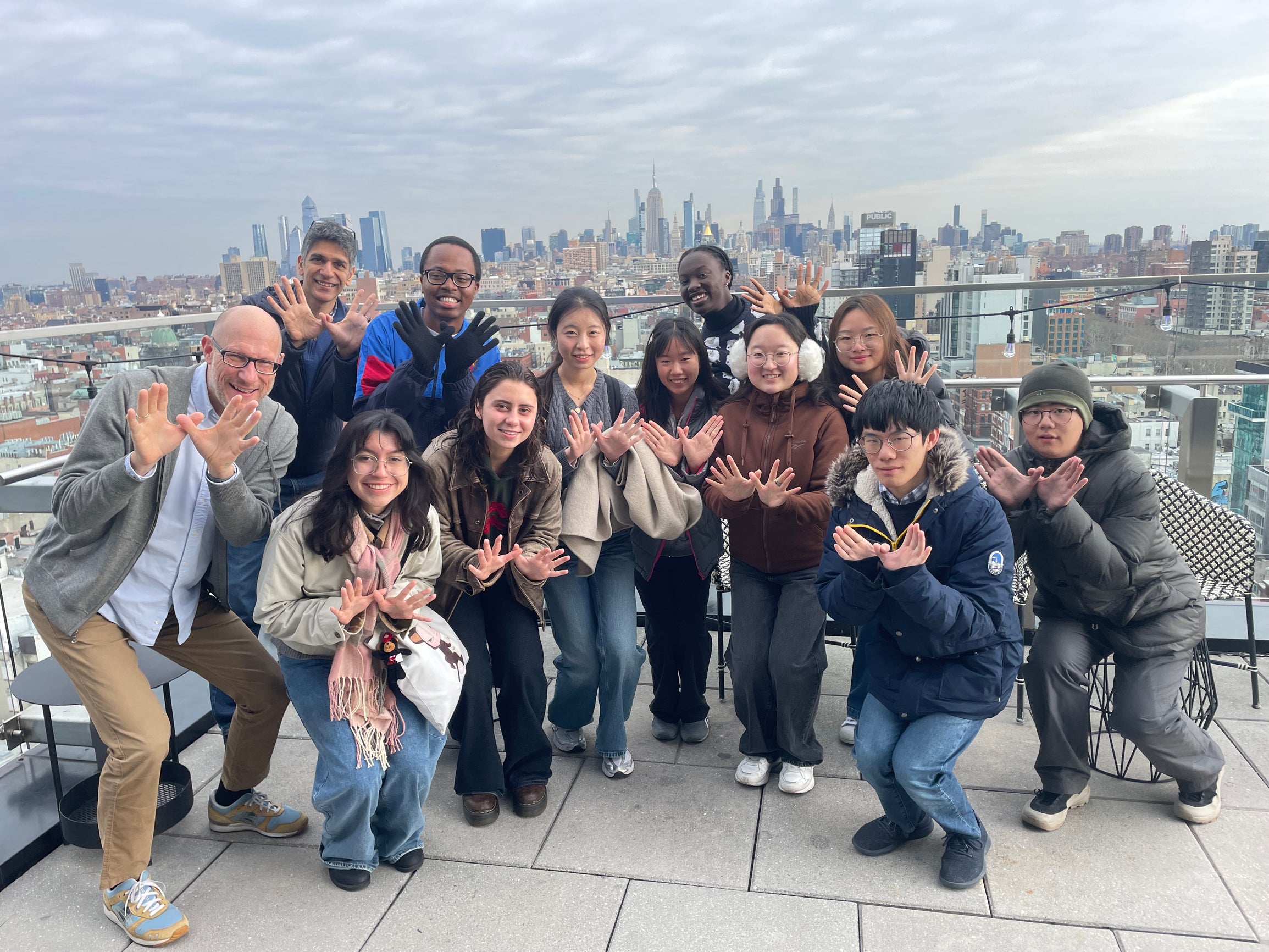 students flashing the Rice University symbol with their hands at the top of building in New York City